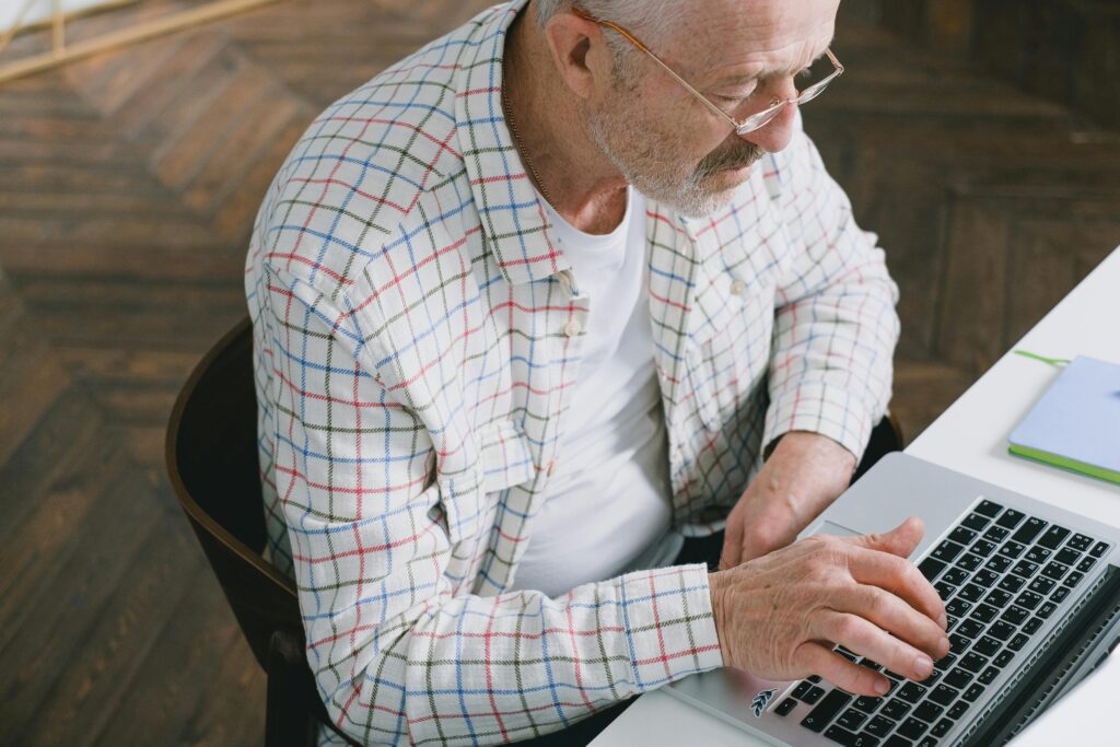 Elderly man using a laptop indoors, showcasing modern technology and digital engagement.