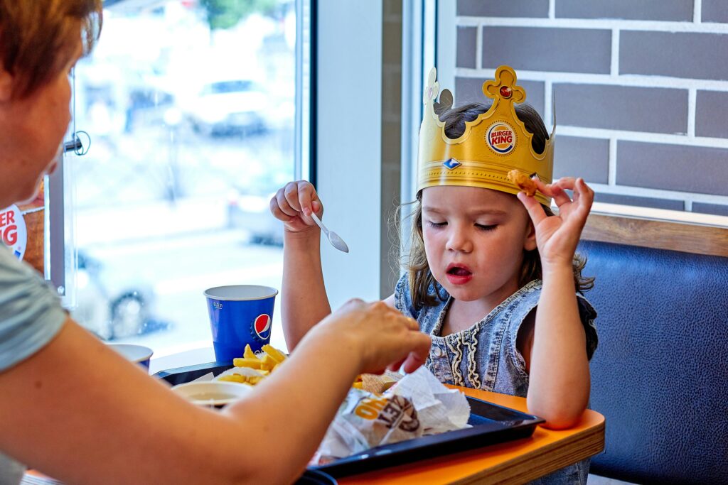 A child wearing a paper crown eats with mother at a fast food restaurant.