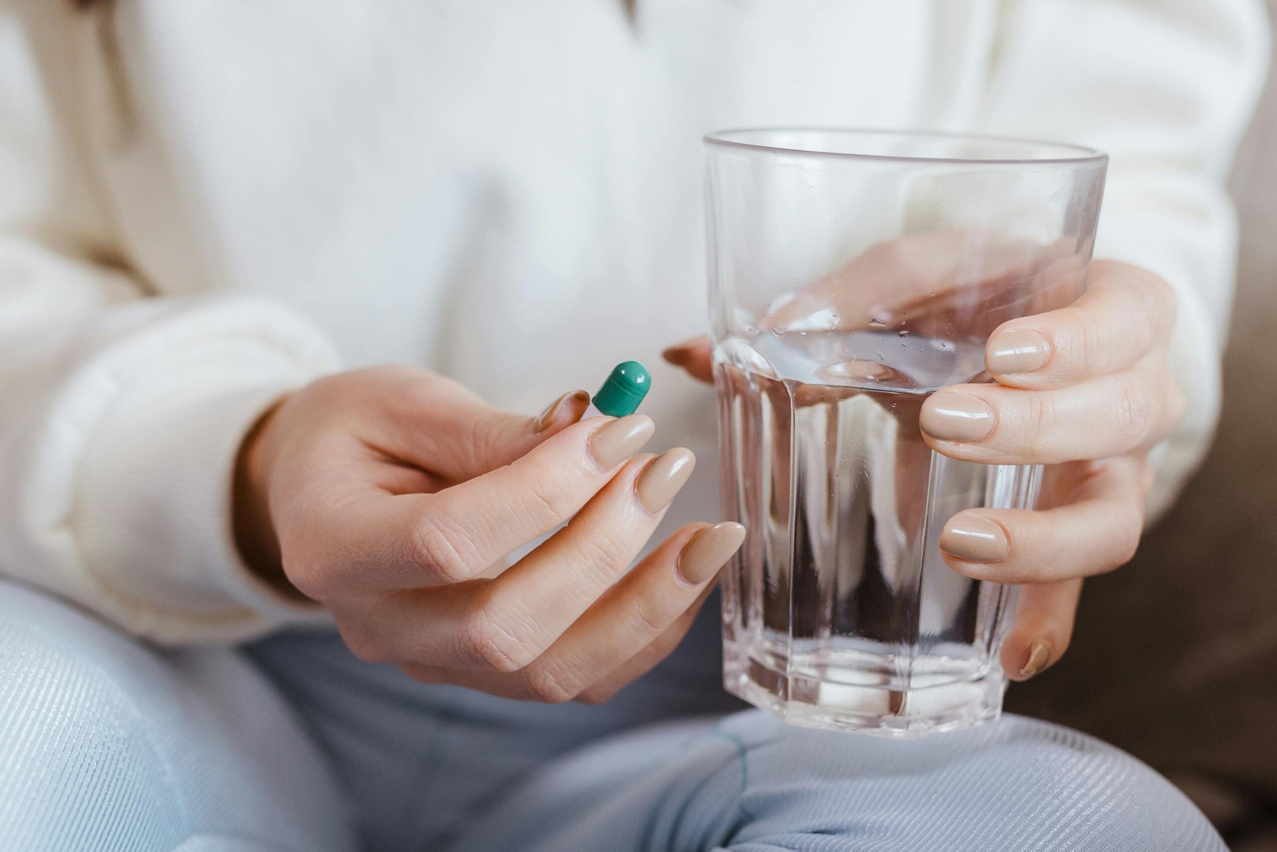 Adult woman hands holding a pill and a glass of water, ready to take medication.