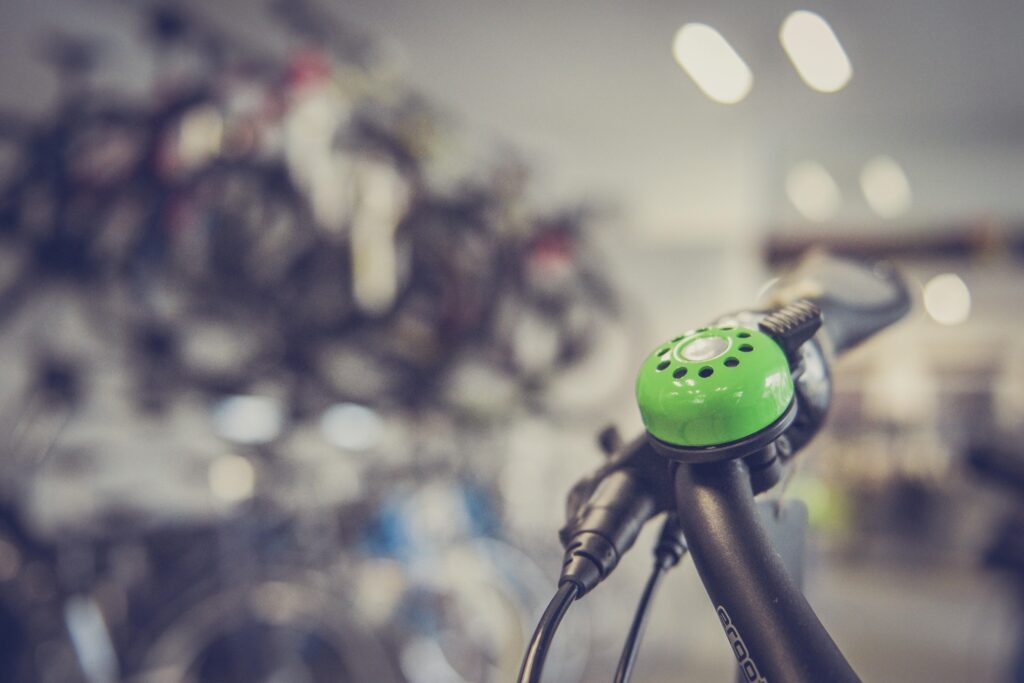 Close-up of a green bicycle bell on handlebars with blurred bike shop in background.