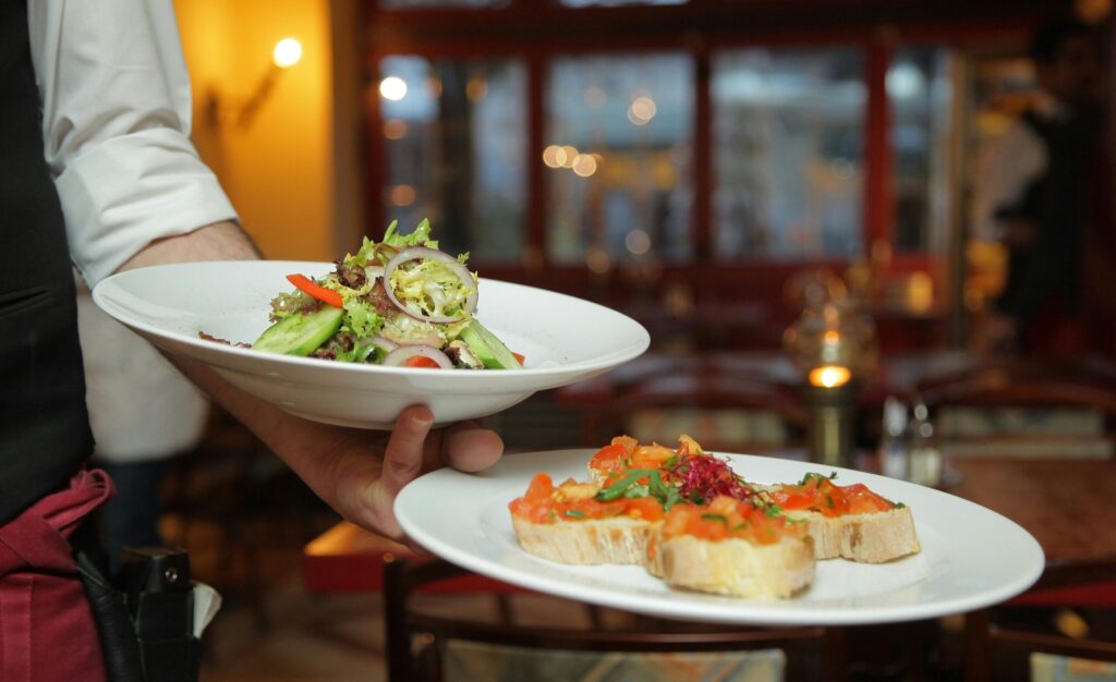 A waiter serves a fresh salad and hors d'oeuvres in a cozy restaurant setting.