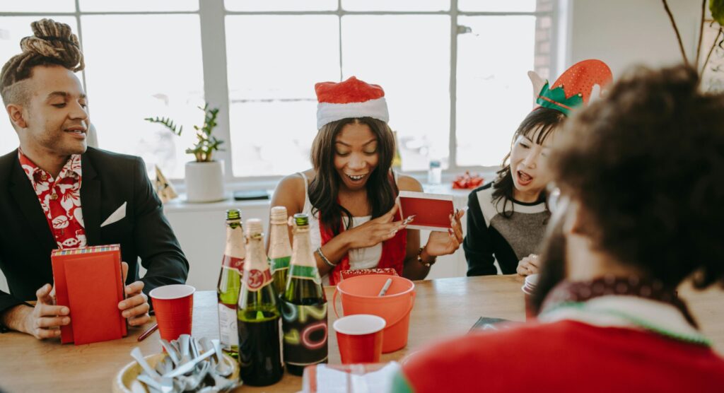 Diverse group of friends celebrating at a holiday party, exchanging gifts and enjoying drinks indoors.