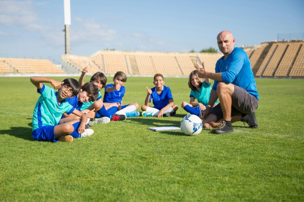 Children enjoying soccer training with coach at an outdoor stadium. Smiles and teamwork on a sunny day.