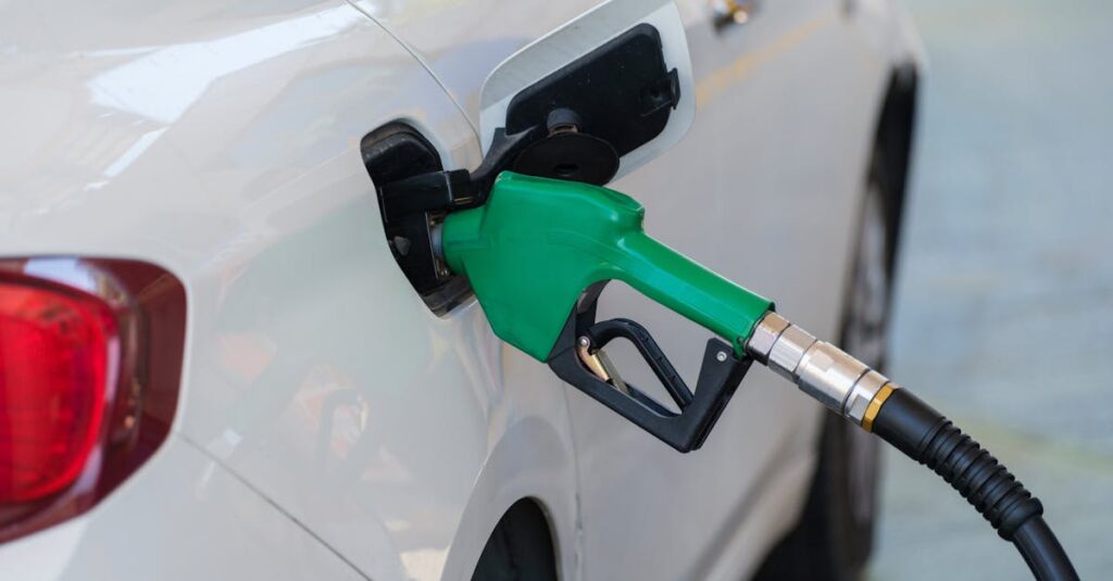 Close-up of a green nozzle refueling a white car at a gas station.