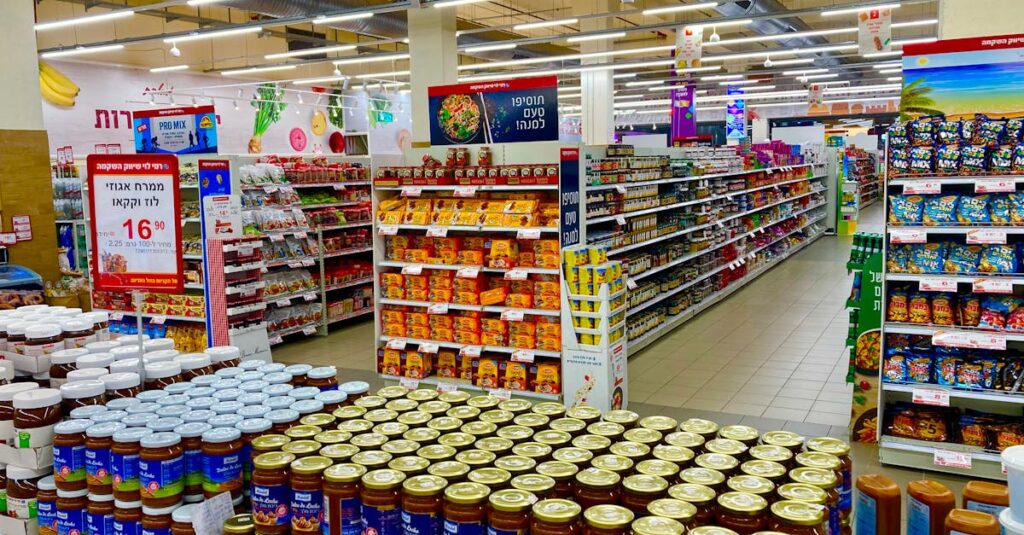Wide view of a fully stocked supermarket aisle with jars and various products on shelves.