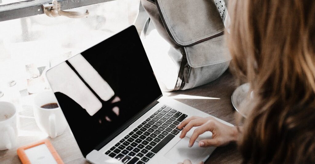 A young woman works remotely at a café, using her laptop and external hard drive.
