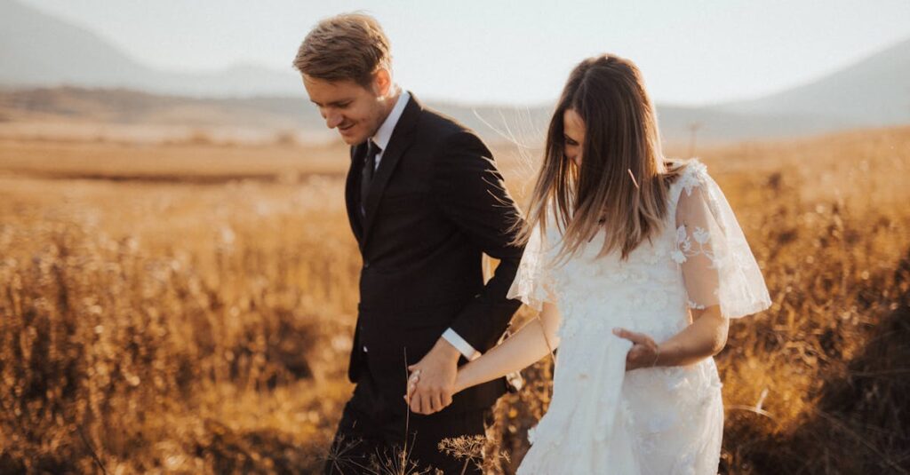 Newlywed couple walking hand in hand through a golden field on their wedding day, exuding love and happiness.