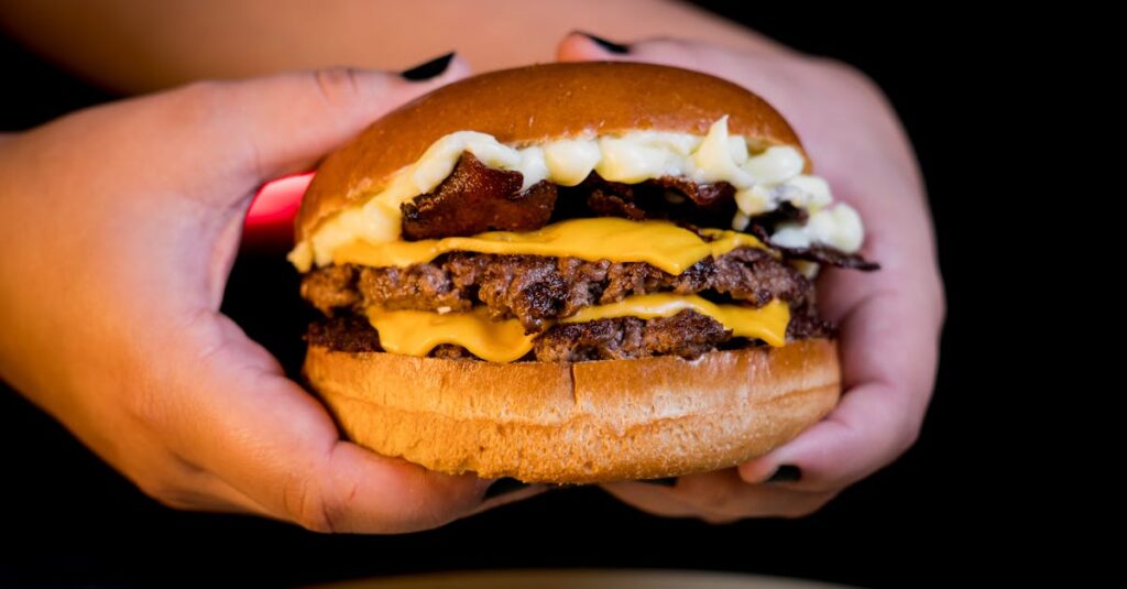 Close-up of a mouthwatering double cheeseburger with bacon, held in hands over a dark background.