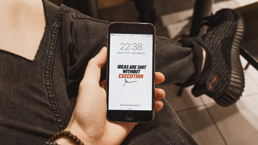 Hand holding iPhone displaying motivational quote. Casual setting with sneakers visible.