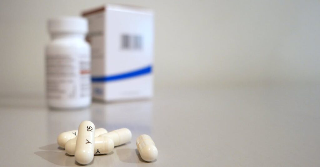 Close-up image of white capsules with medicine bottle and box in the background.