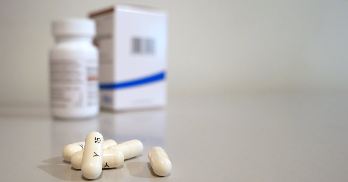 Close-up image of white capsules with medicine bottle and box in the background.
