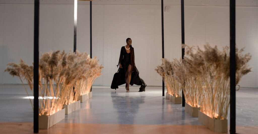 Graceful model in a black dress walking on a runway indoors, surrounded by minimalist decor.